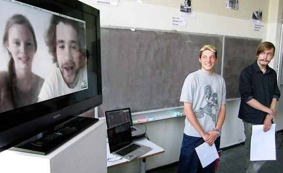Students in front of class and on monitor in front off class give a presentation